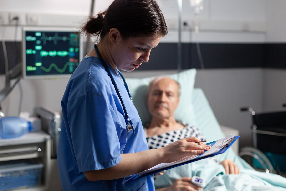 Nurse caring for elderly patient at bedside with real-time clinical monitoring
